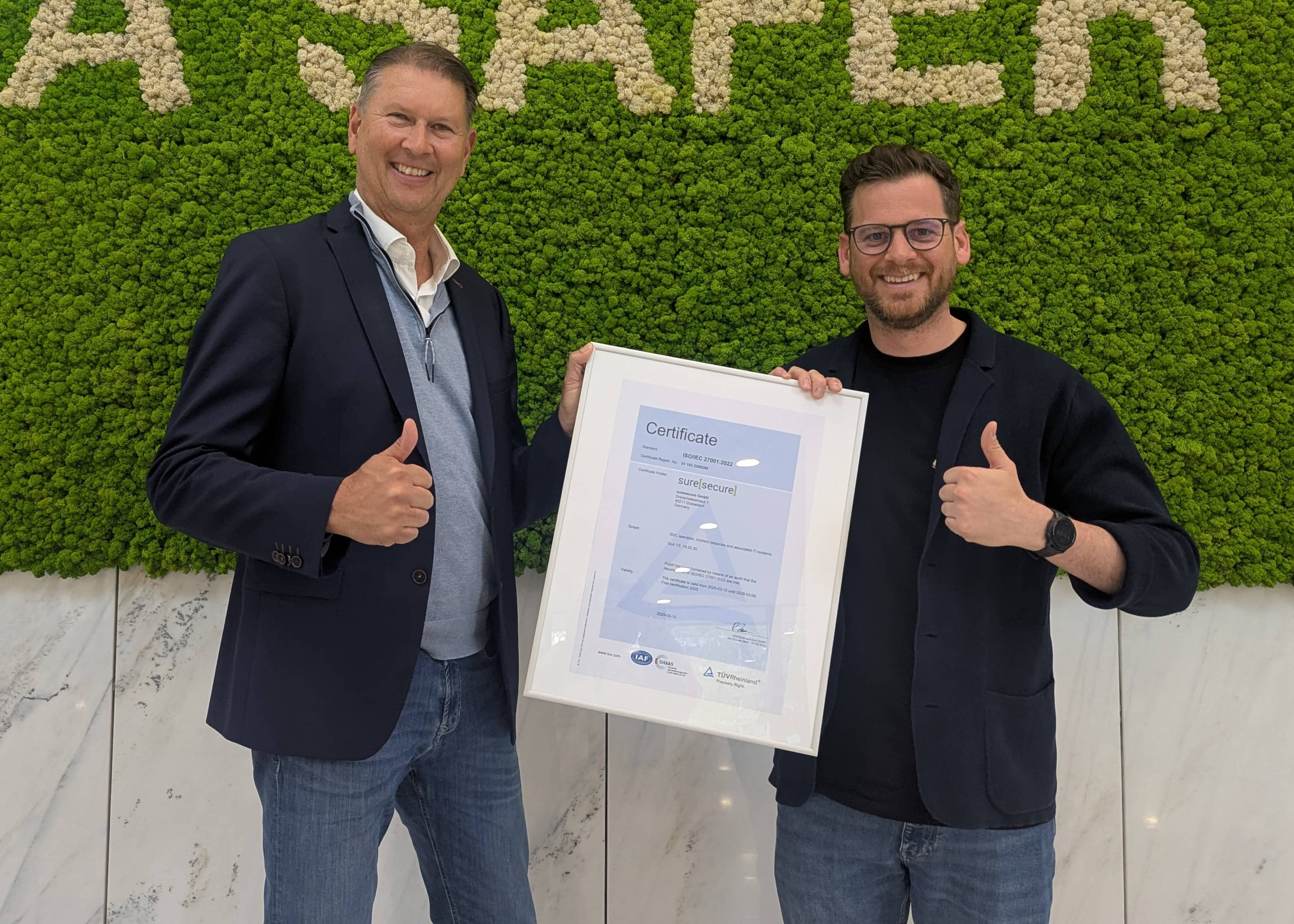 Michael Döhmen and a representative from TÜV Rheinland hold up the suresecure ISO certificate.